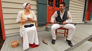 A male and female historical reenactor are sitting in chairs on the porch of the Lavalle House.